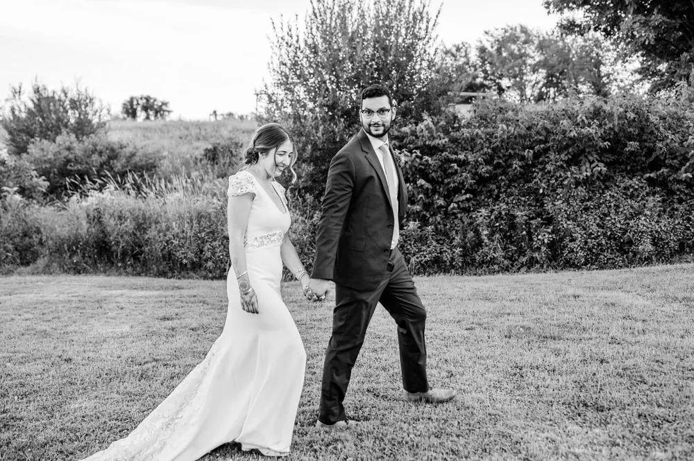 The couple walk hand in hand across a field, in black and white