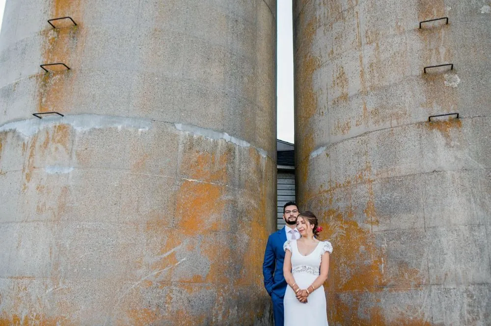 The couple stand small between 2 weathered, rust-streaked silos