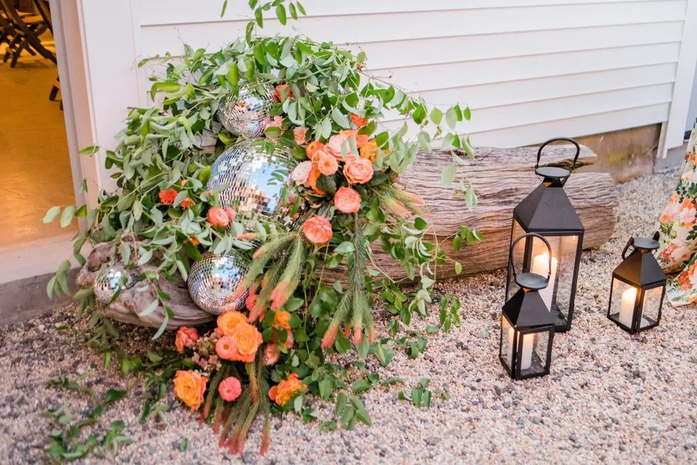 Disco balls tucked into orange flowers and greenery beside black lanterns