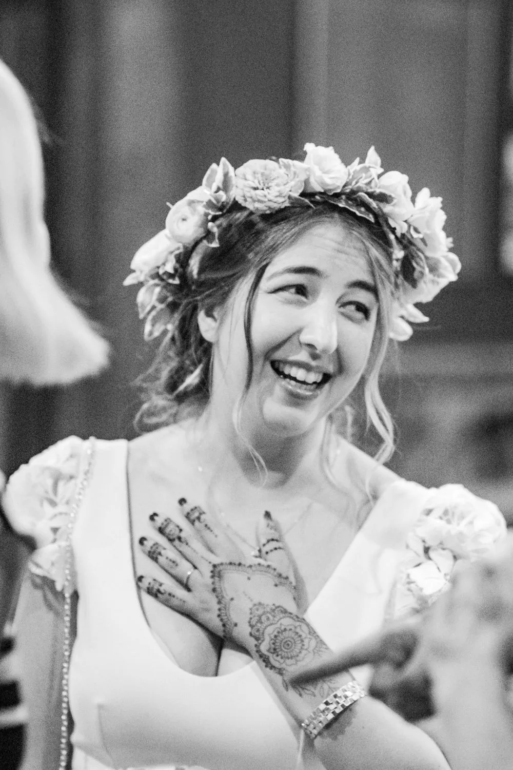 The bride laughs in a flower crown, henna on her hands, in black and white