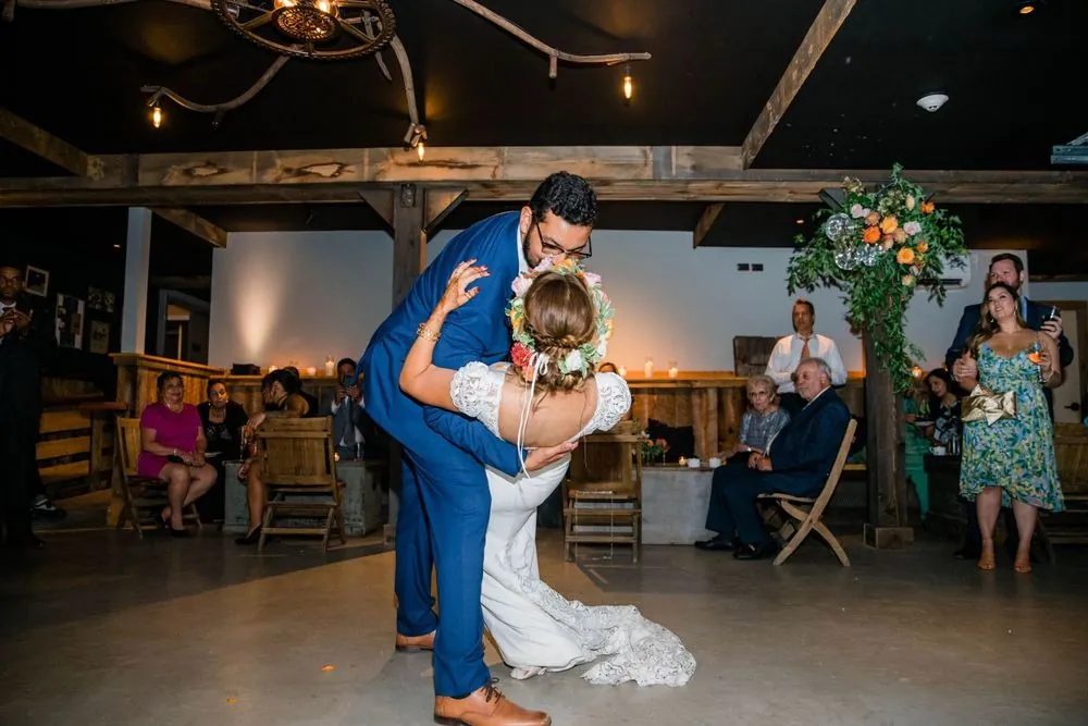 The groom dips the bride low on the barn dance floor as guests watch