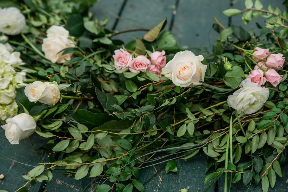 Close view of white and blush roses woven through the greenery arch