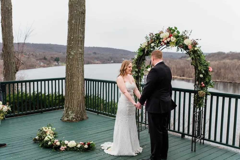 A wide view of the couple under the rose arch with the river and hills beyond