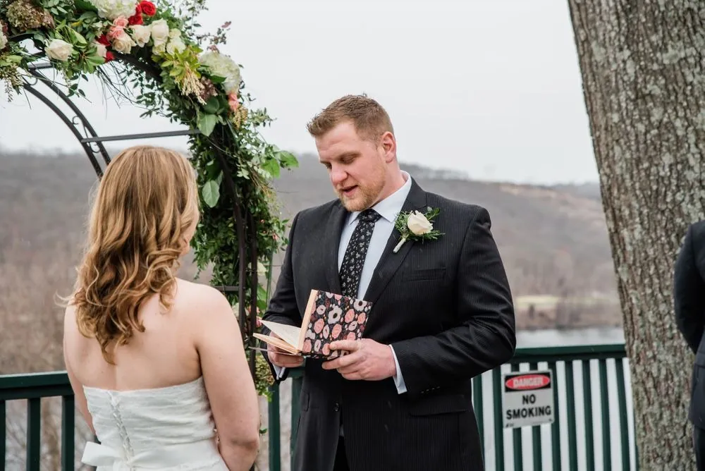 The groom reads his vows from a small card as the bride listens