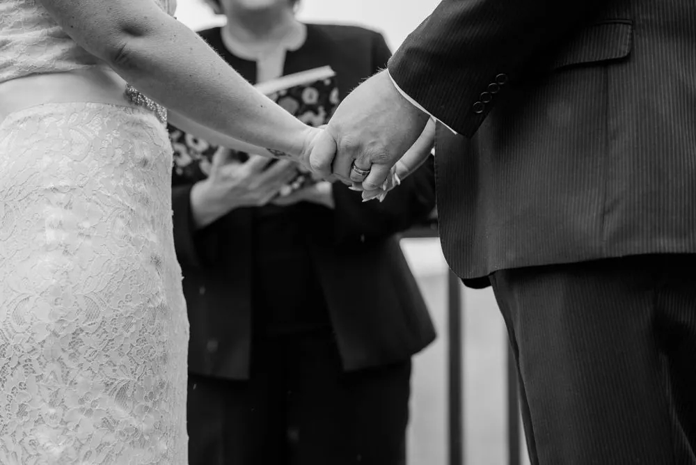 Black and white close view of the couple's joined hands during the vows