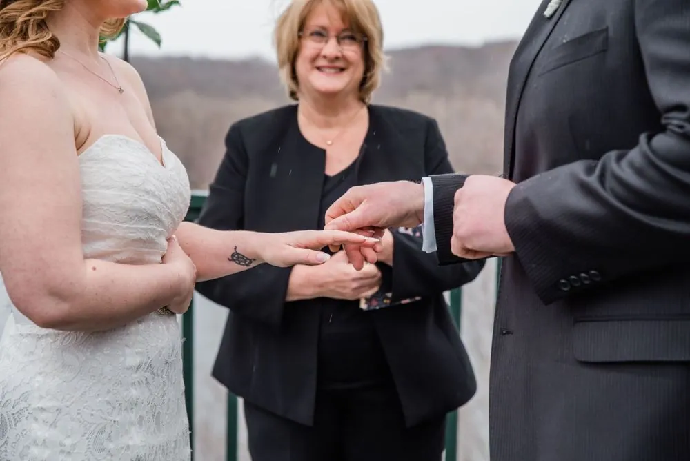 The groom slides a ring onto the bride's finger as the officiant smiles