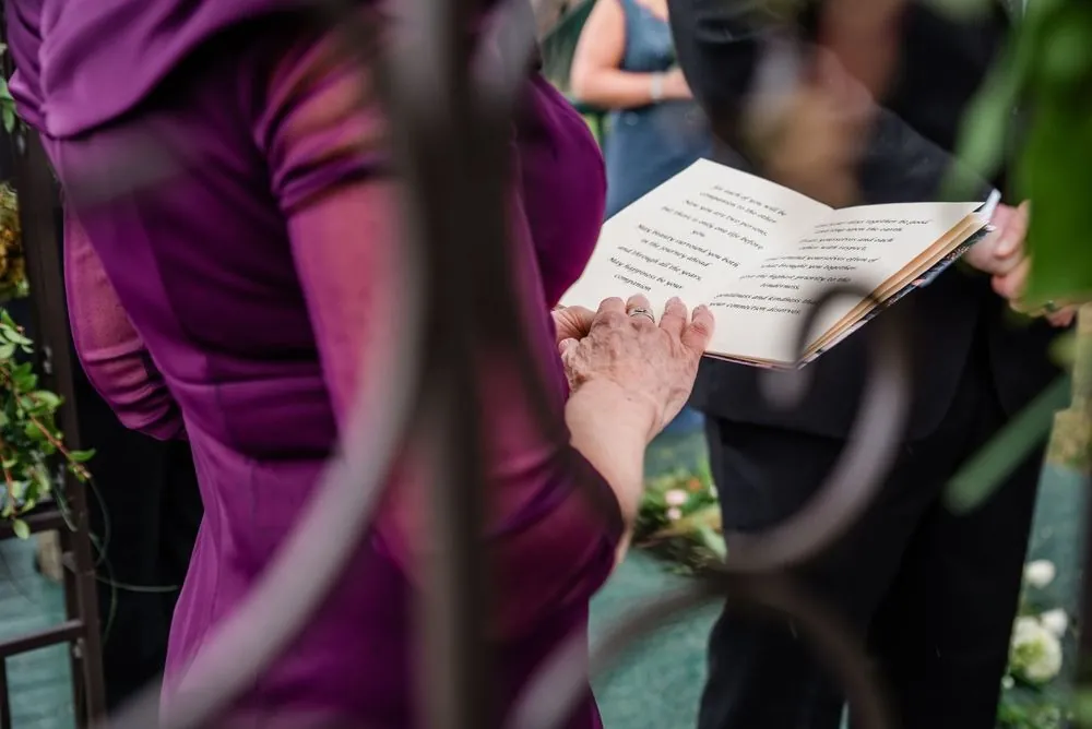 A guest in plum reads from a booklet during the ceremony