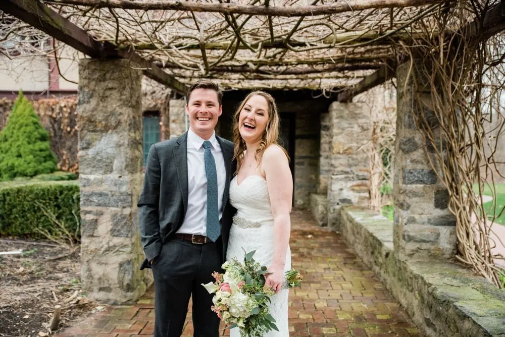 The couple laughs together under the pergola beside the stone columns