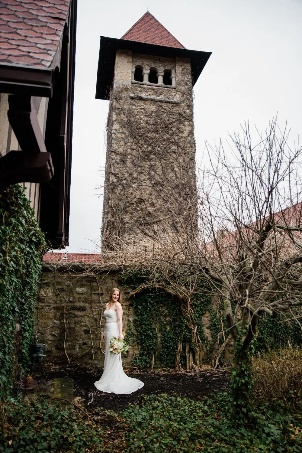 The bride stands small at the base of the castle's stone tower