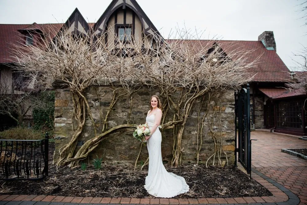 The bride holds her bouquet beside a stone wall covered in bare vines