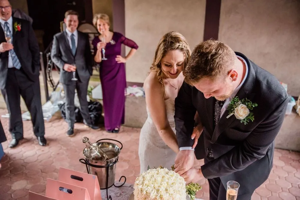 The bride and groom cut a small round cake as family looks on