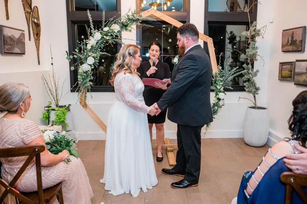 The couple holds hands facing each other under the rose-covered arch