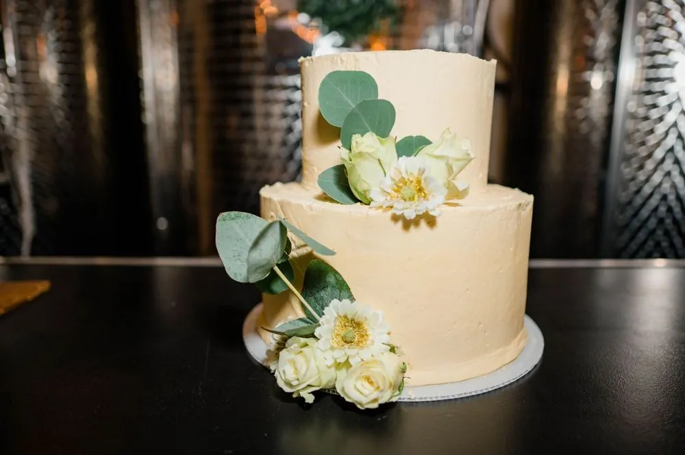 A 2-tier ivory buttercream cake with white roses on a dark table
