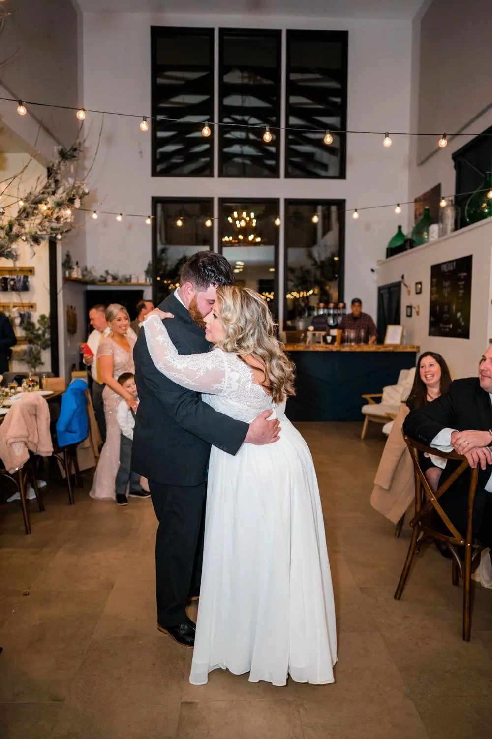 The couple slow dances under string lights as guests smile from their seats