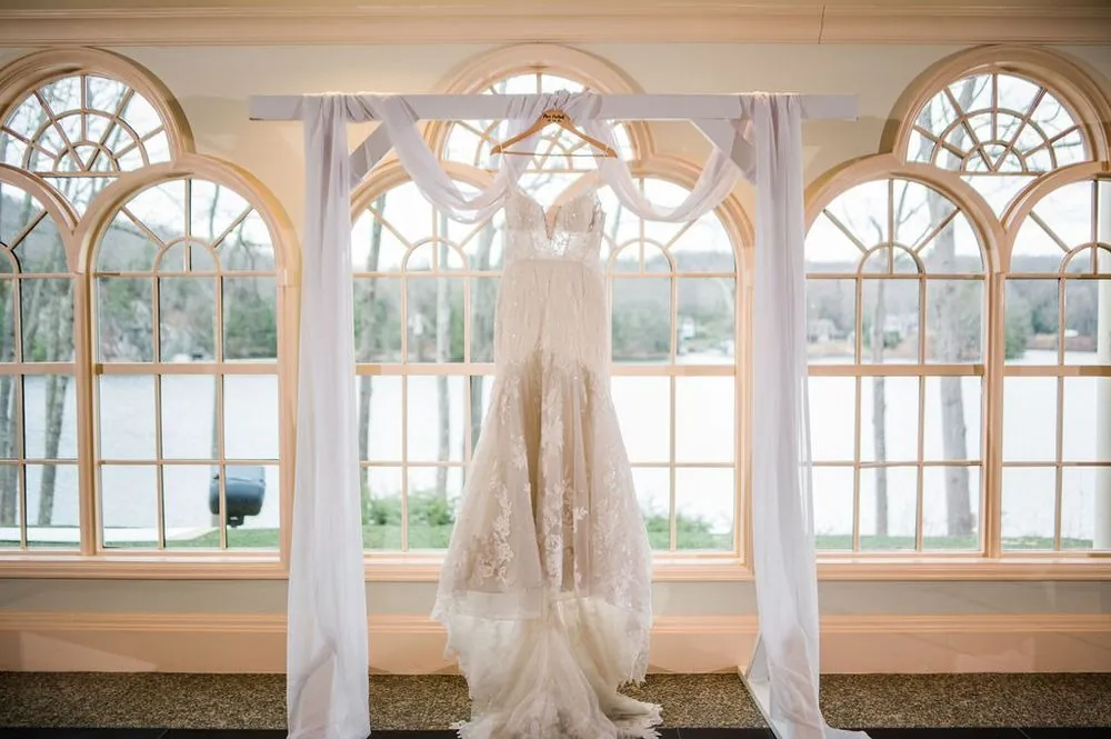 The lace gown hangs framed by sheer curtains in arched windows overlooking the water