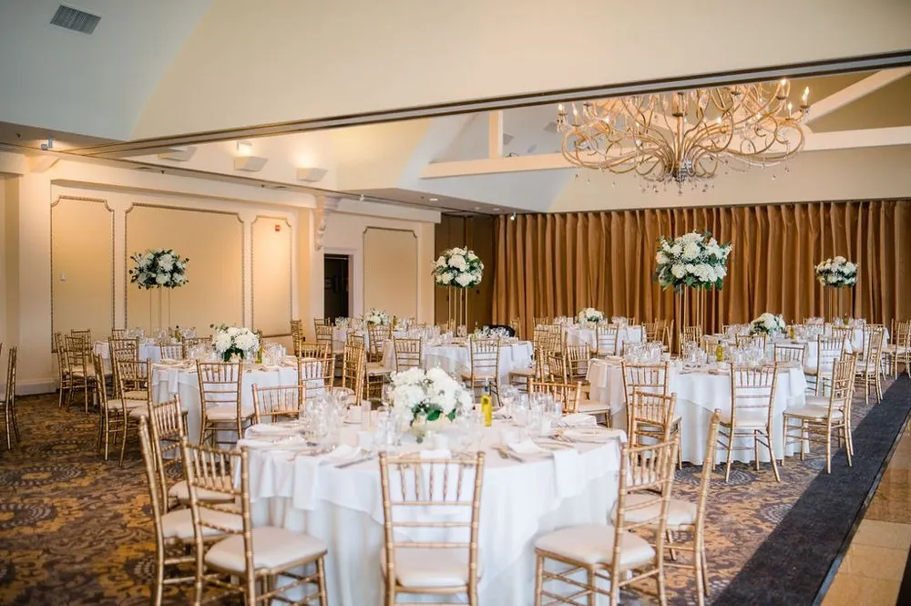 The ballroom set with gold chairs, white linens and tall white floral centerpieces
