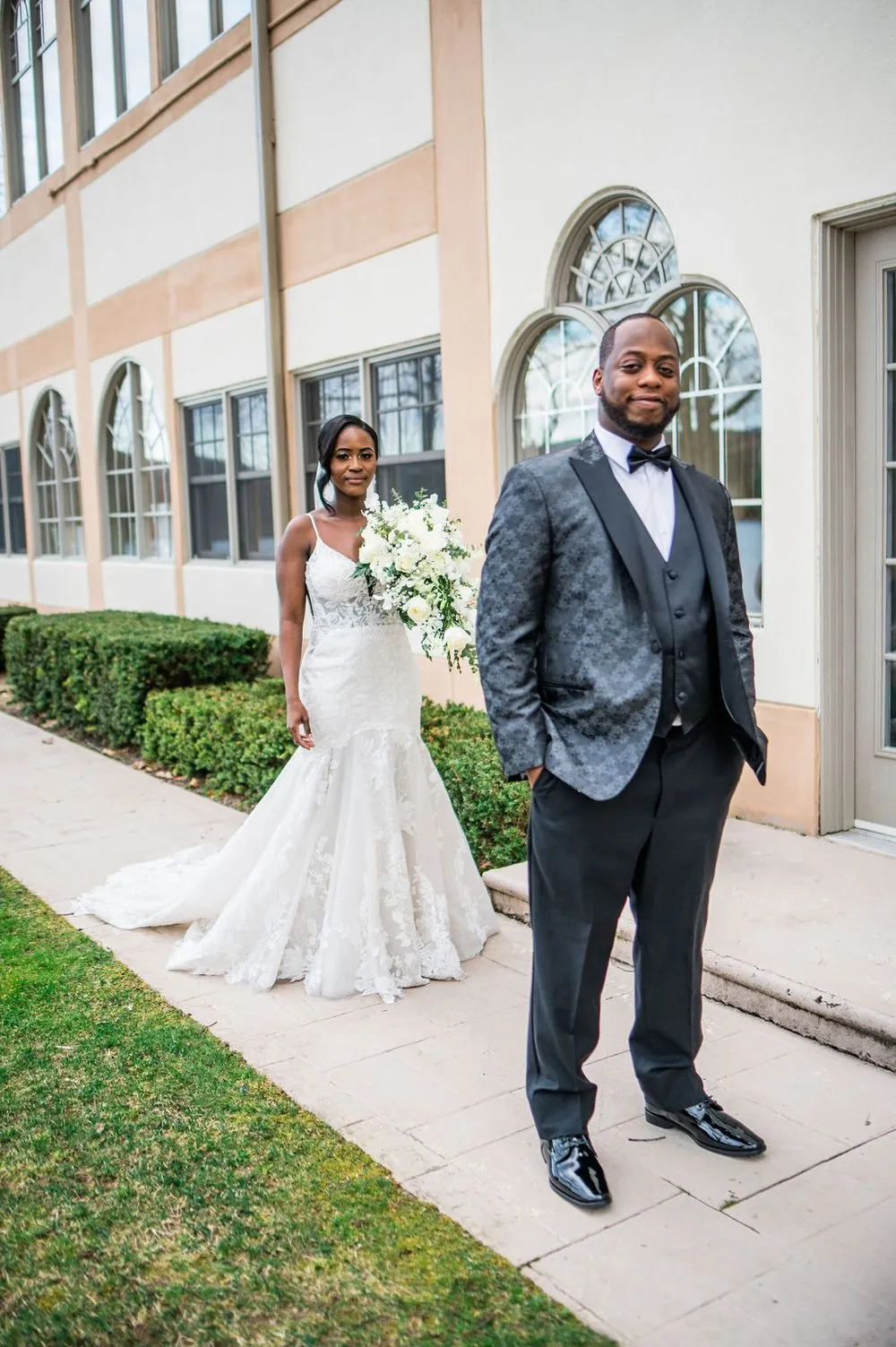 Taria and Franklin face each other on a hedge-lined path during their first look
