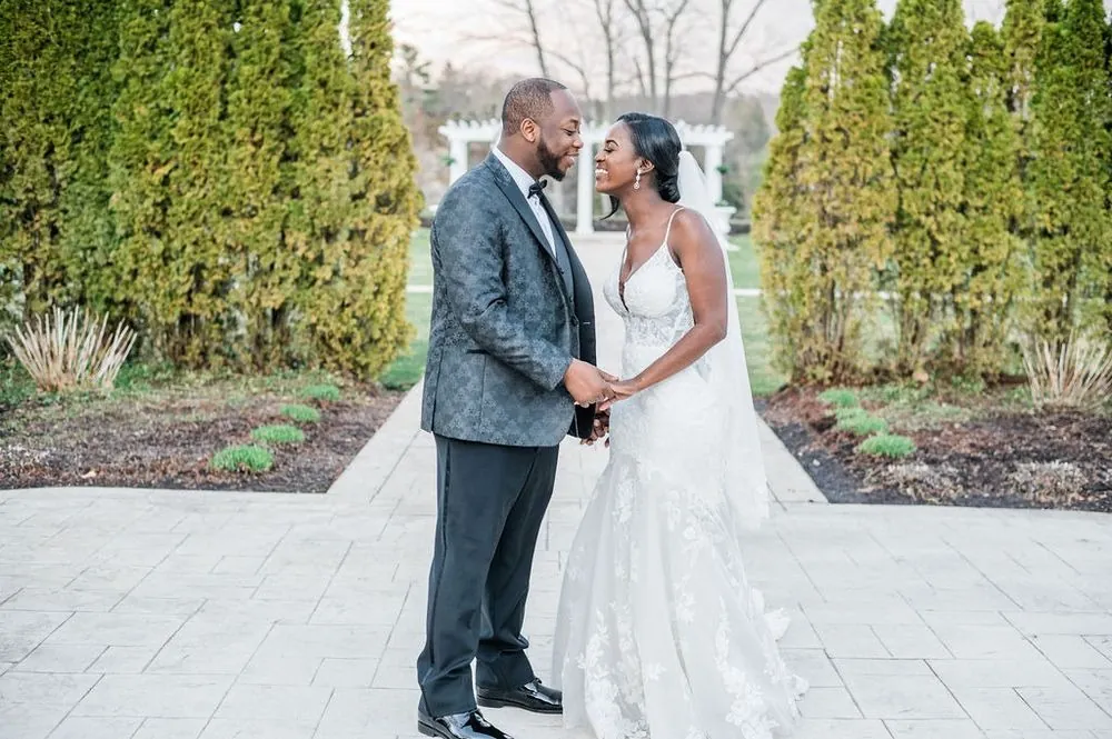 Taria and Franklin laugh face to face on a stone path in front of a white pergola