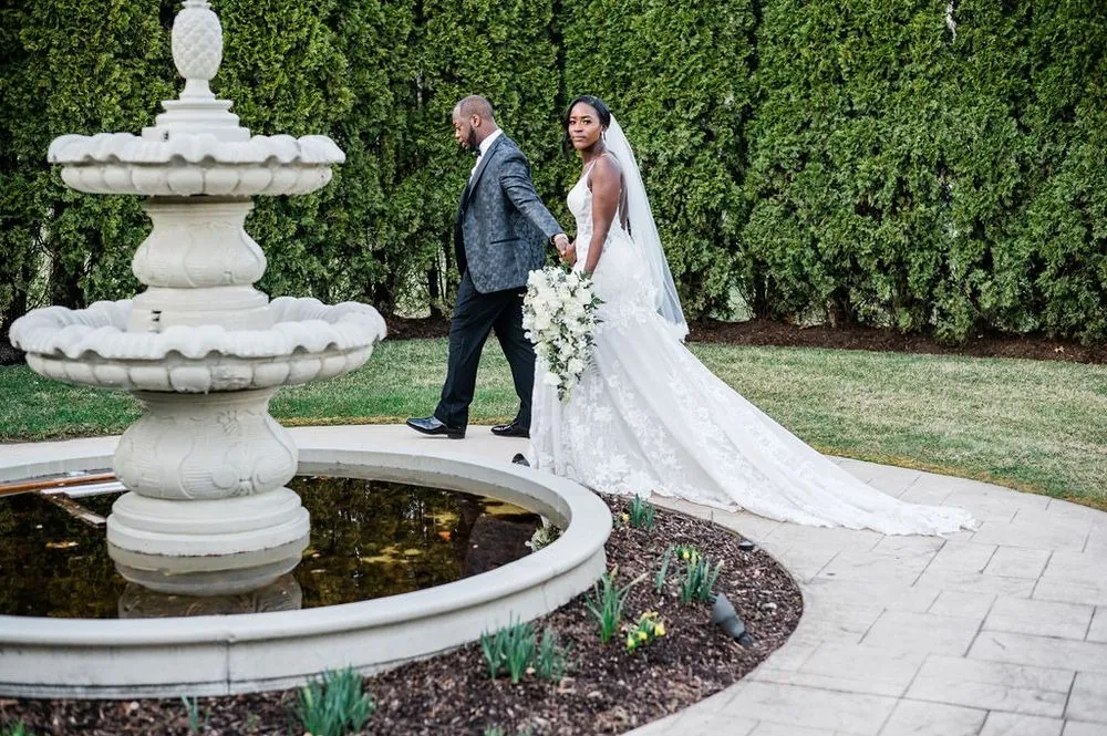 Franklin leads Taria past a tiered stone fountain, her long lace train trailing behind