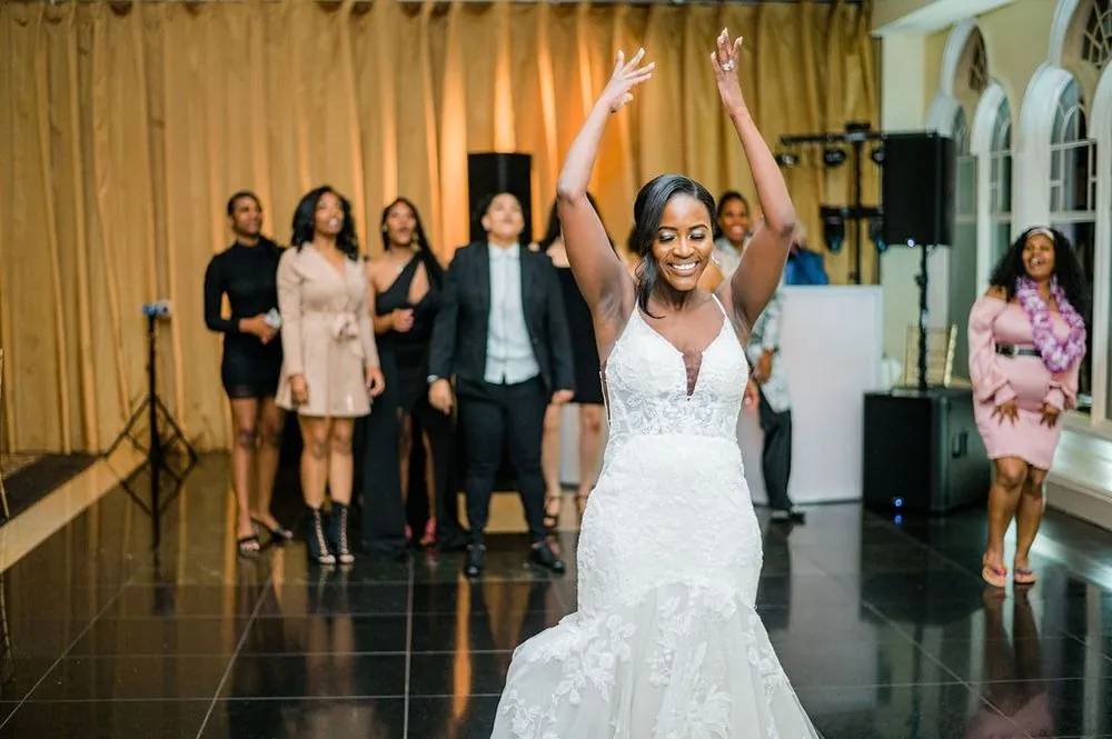 The bride throws both arms up on the dance floor as friends dance around her