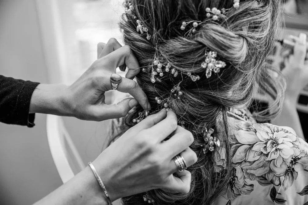 Hands tuck dried flowers into the bride's braided hair, in black and white