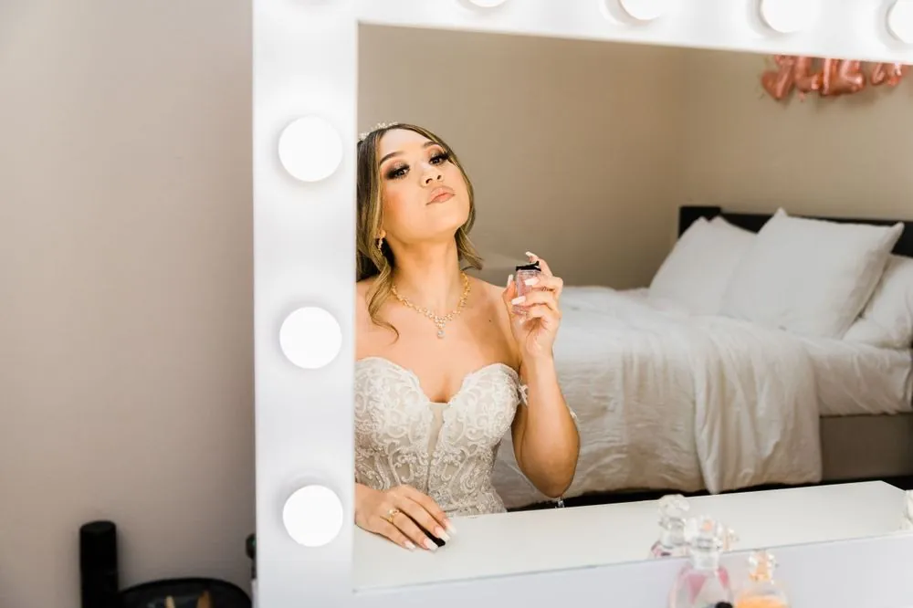 The bride in her gown checks her reflection in a lit vanity mirror