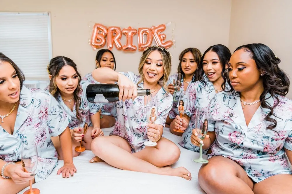Bridesmaids in floral robes crowd onto the bed around the bride under a BRIDE banner