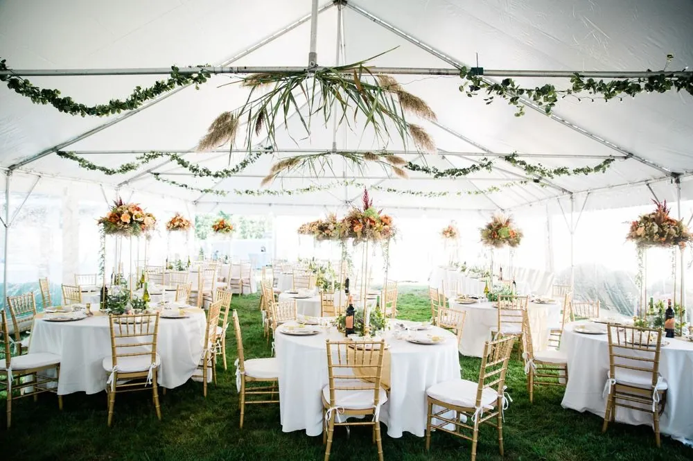 A clear-topped tent with round tables in white and mustard and hanging greenery