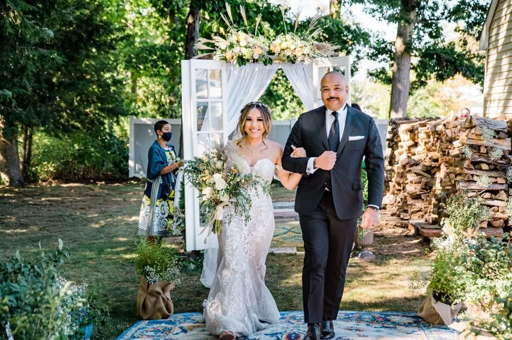 The bride walks the rug aisle on the arm of a man in a black suit