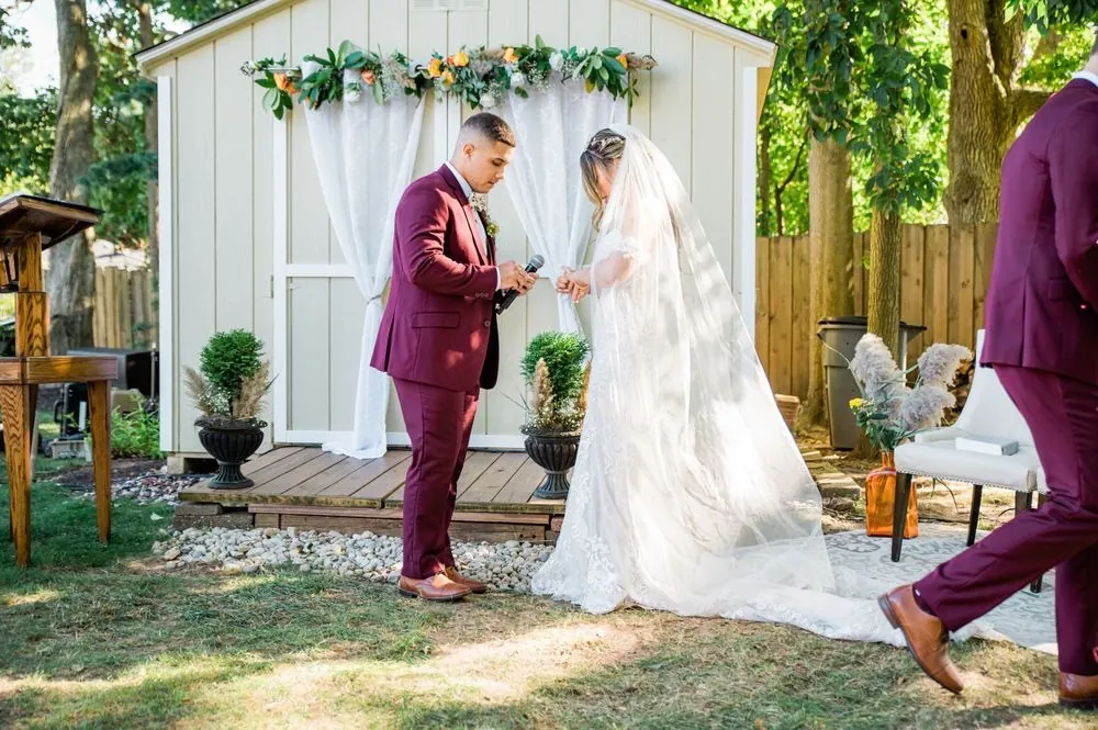 Tyler holds a microphone as he and Tatiana exchange rings in front of the dressed shed