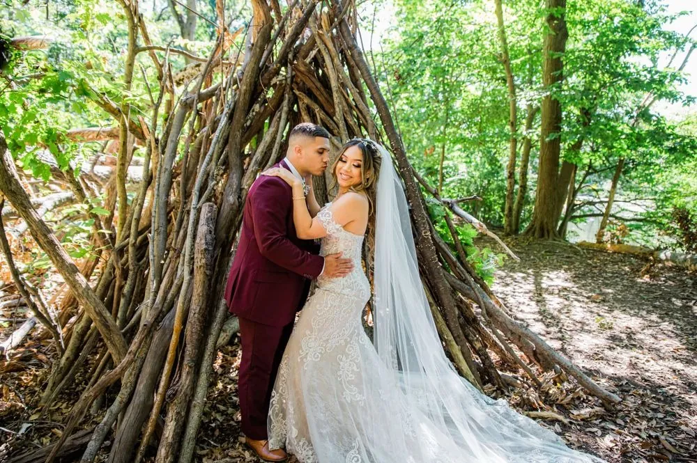 Tyler kisses Tatiana's temple inside a stick teepee in the woods, her veil pooling on the leaves