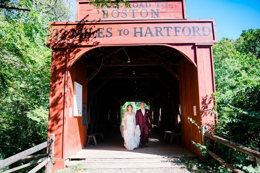 Tatiana and Tyler stand inside the mouth of a red covered bridge