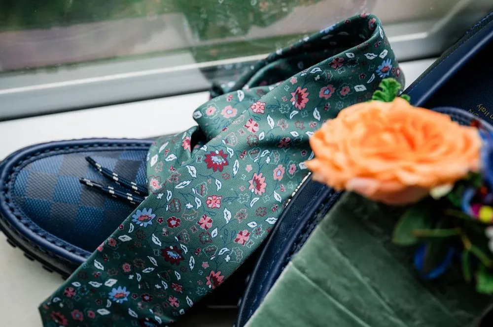 Green floral tie, navy shoes and an orange rose boutonniere laid out together