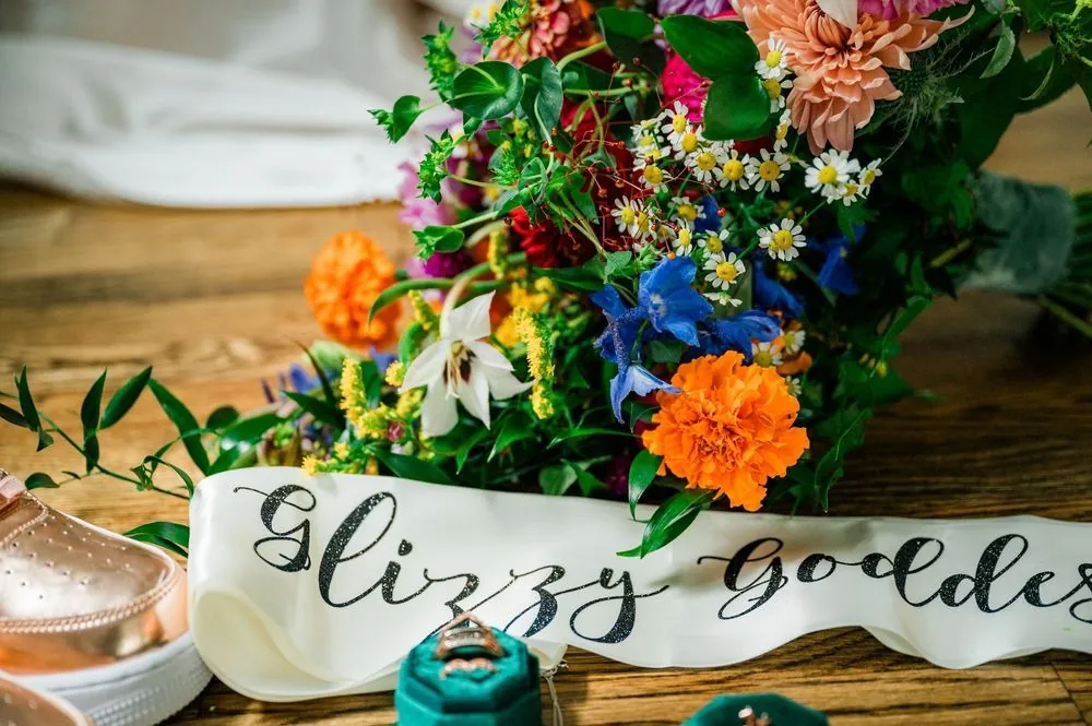 Rainbow bouquet of marigolds and delphinium beside a Glizzy Goddess satin sash