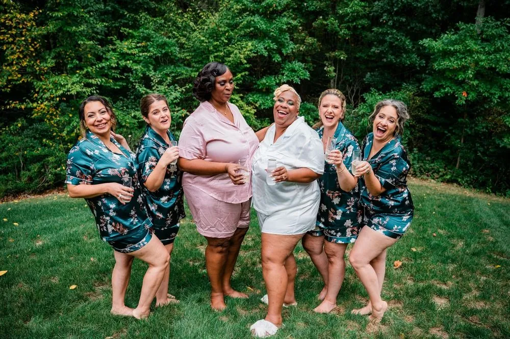 The bride and her friends in matching robes laugh together on the lawn