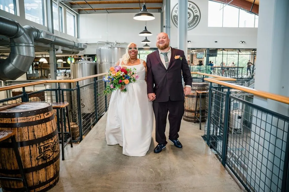 Tiffanie and Kevin stand arm in arm on the catwalk beside wooden barrels