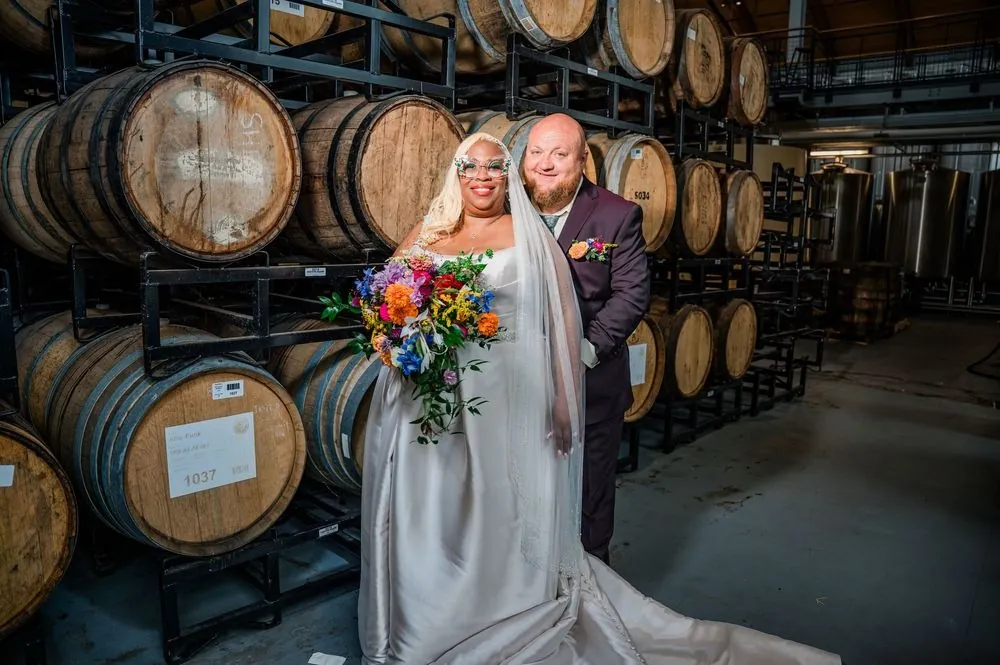 Tiffanie and Kevin pose among towering racks of oak barrels in the warehouse