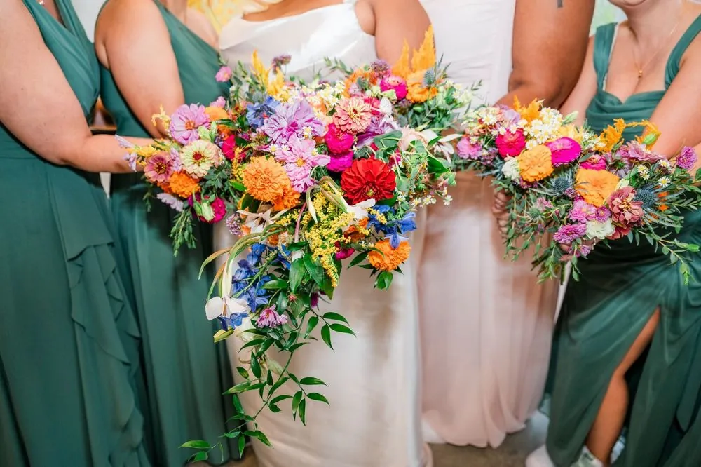 Close view of bridesmaids in green holding bright rainbow bouquets