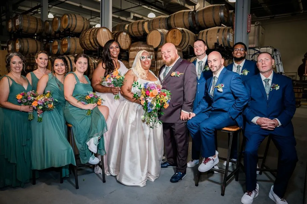 The wedding party gathers in front of barrel racks in green and blue