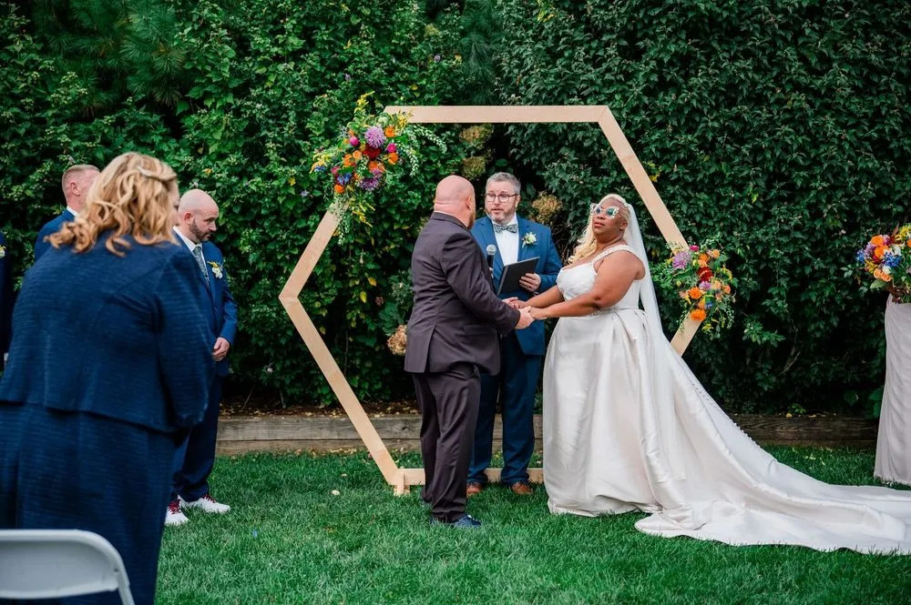 The couple faces each other under a wooden hexagon arch hung with flowers
