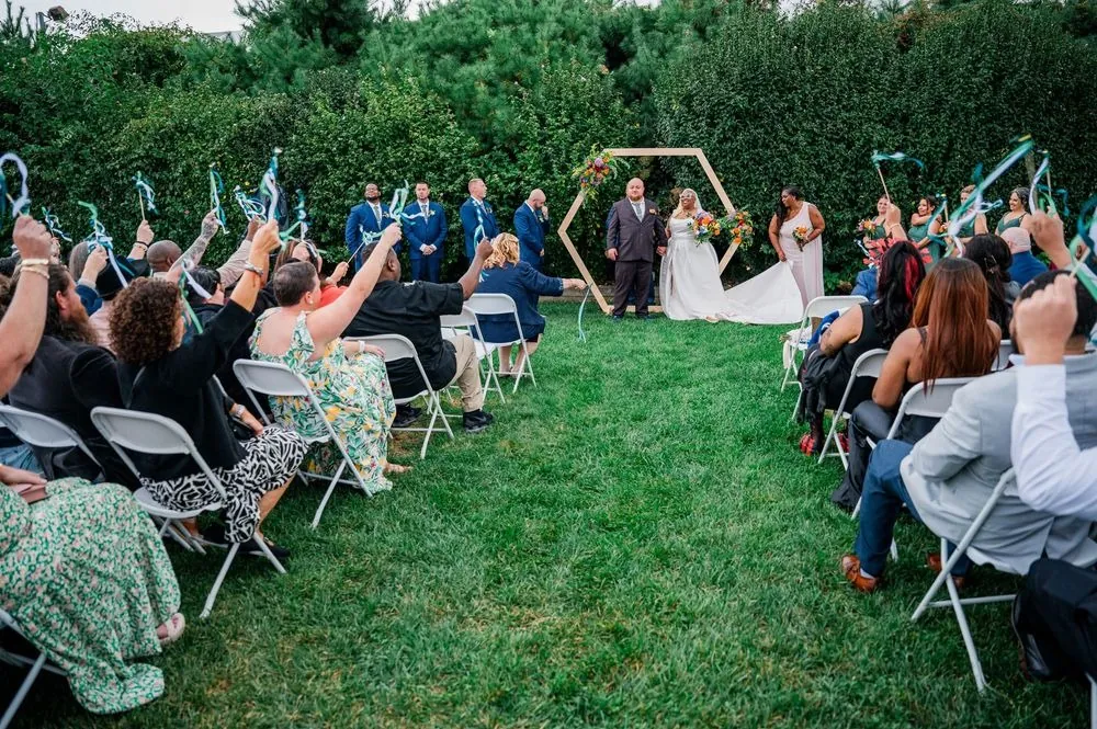 Guests wave ribbon wands as the couple stands at the arch on the lawn