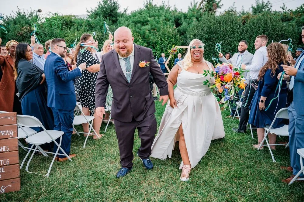 Tiffanie and Kevin walk back up the lawn aisle as guests wave ribbon wands