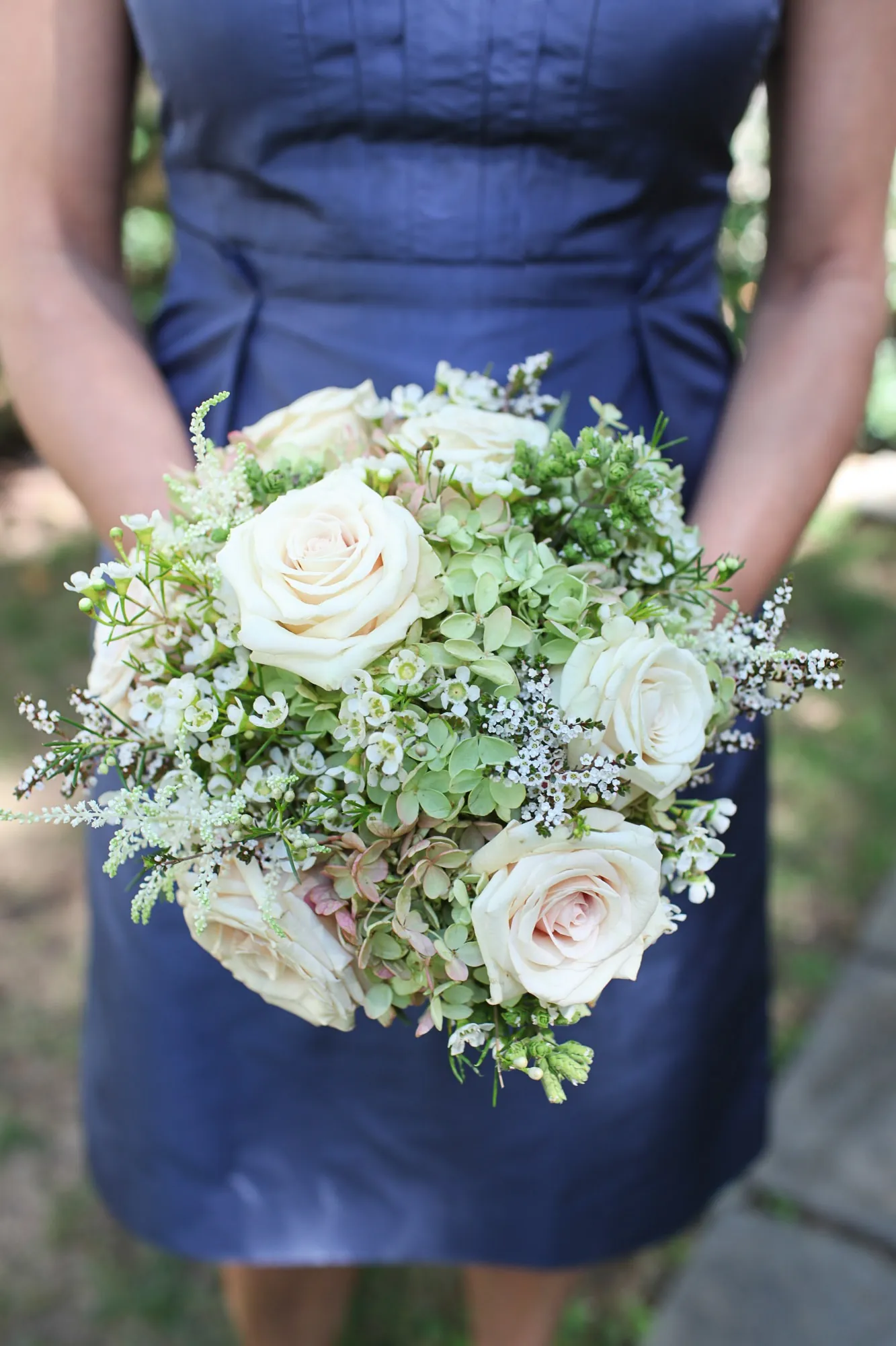 A bridesmaid in navy holds a bouquet of white roses and dusty green foliage
