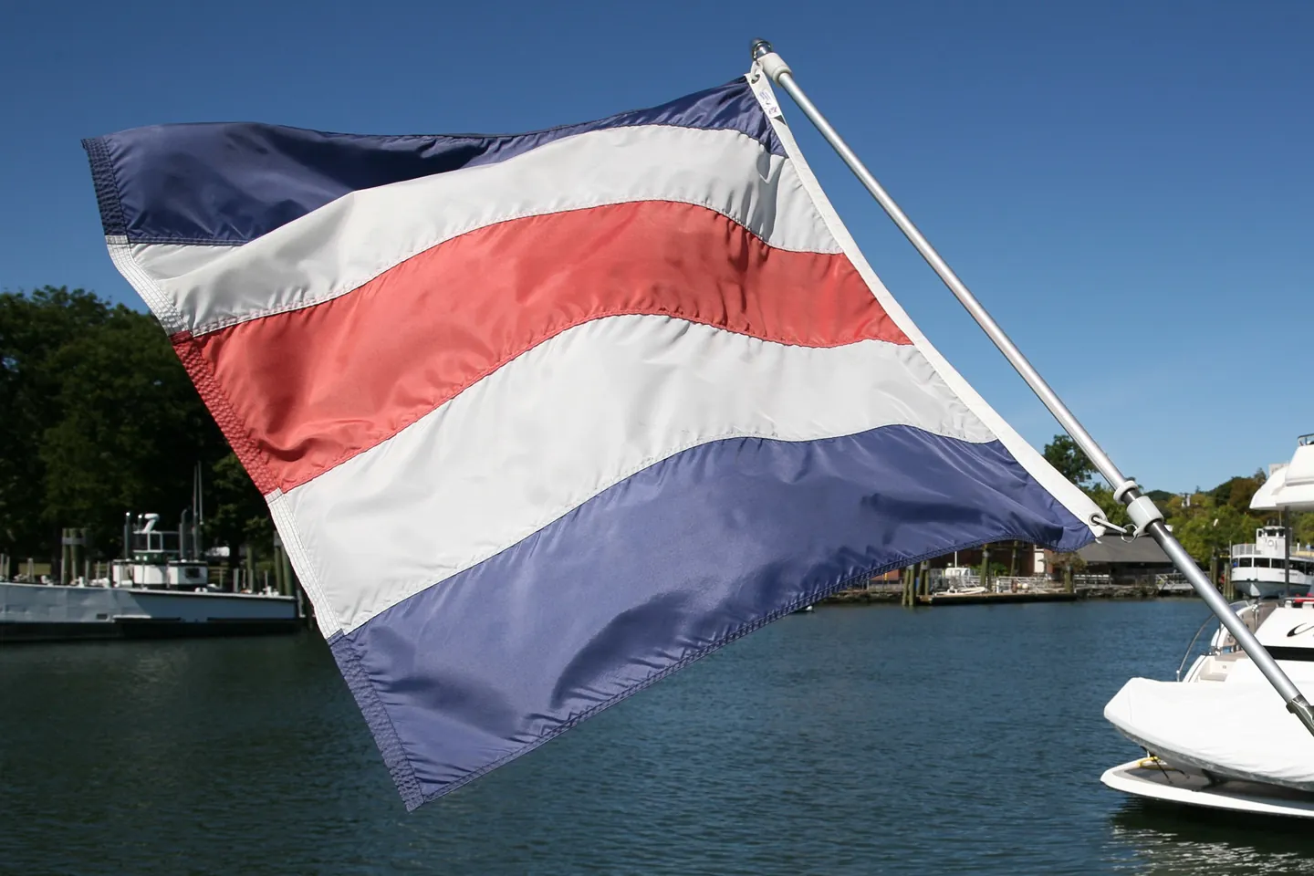 A red, white and blue striped signal flag flies over the harbor and moored boats