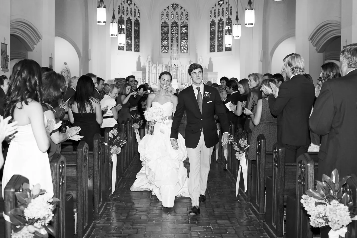 Black and white recessional down the church aisle past guests standing in the pews