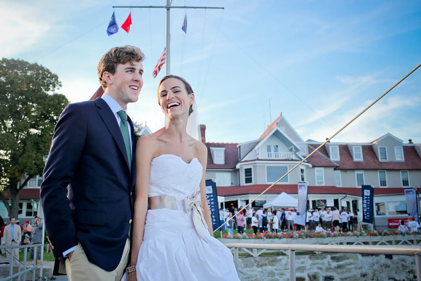 Trevor and Christina laugh on the lawn in front of the white clubhouse under a blue sky