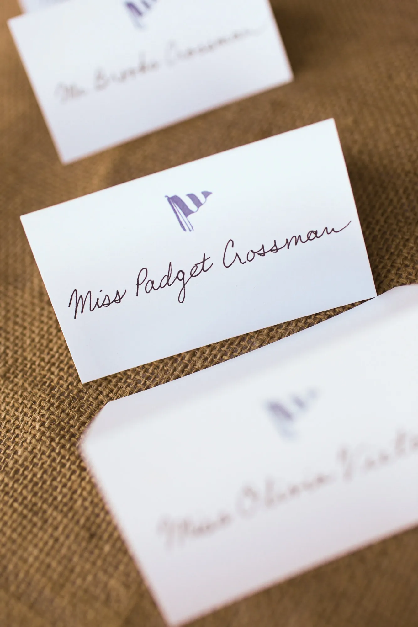 Hand-lettered escort cards with small blue sailboats laid on burlap