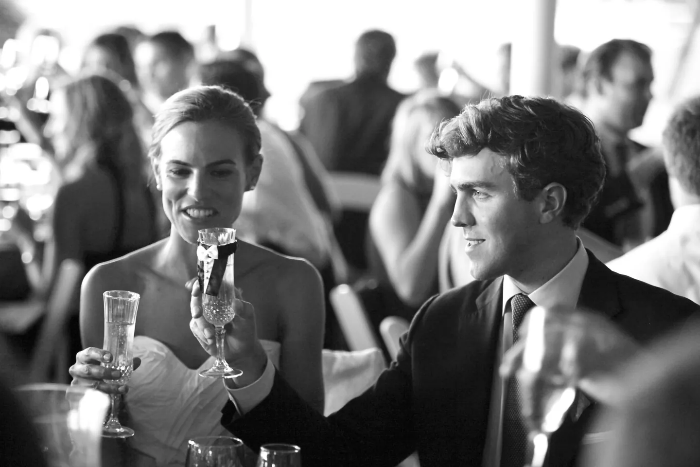 Black and white frame of the couple raising glasses and smiling during toasts