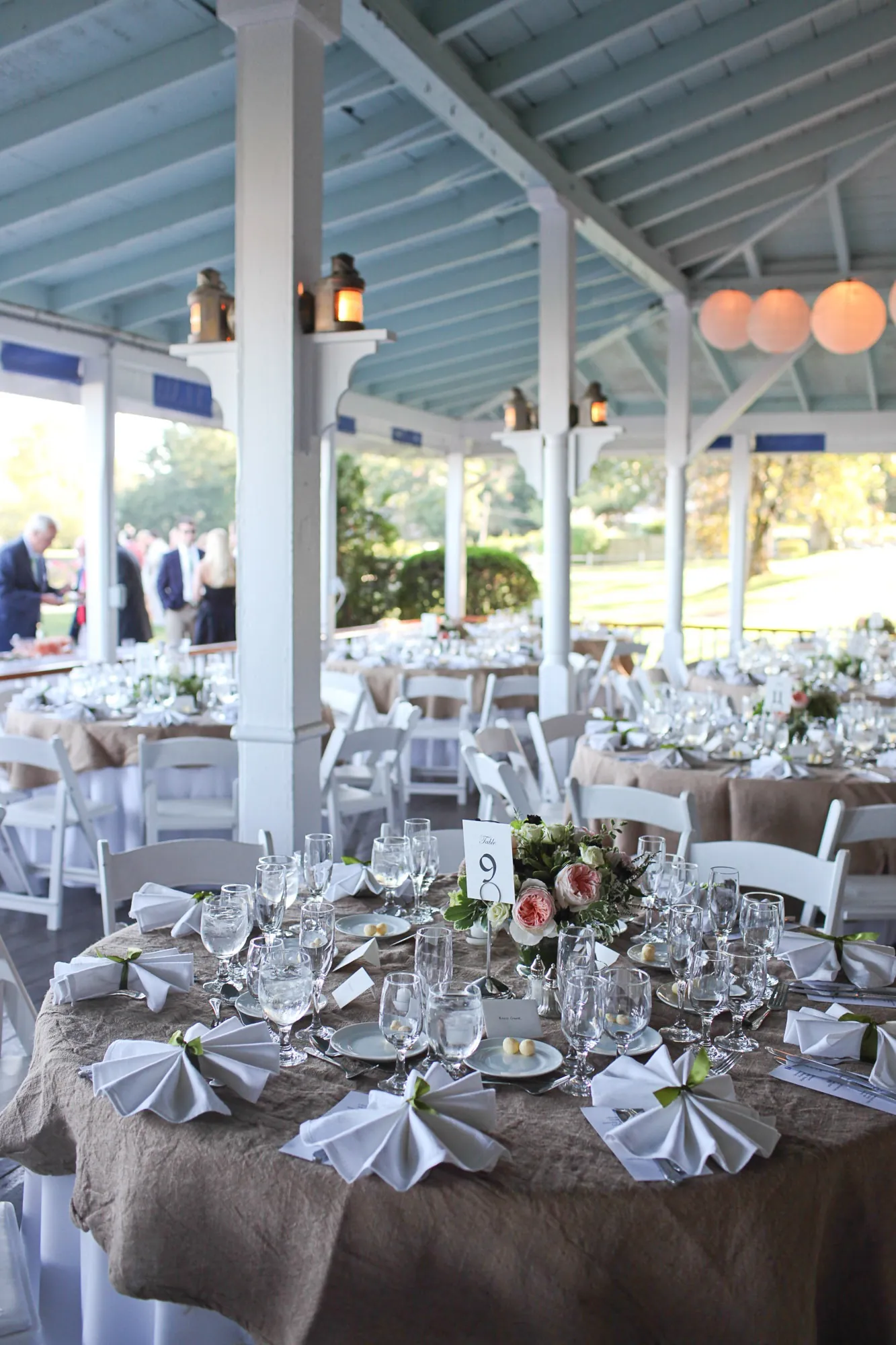 Round tables in burlap and white linen set beneath the pavilion rafters