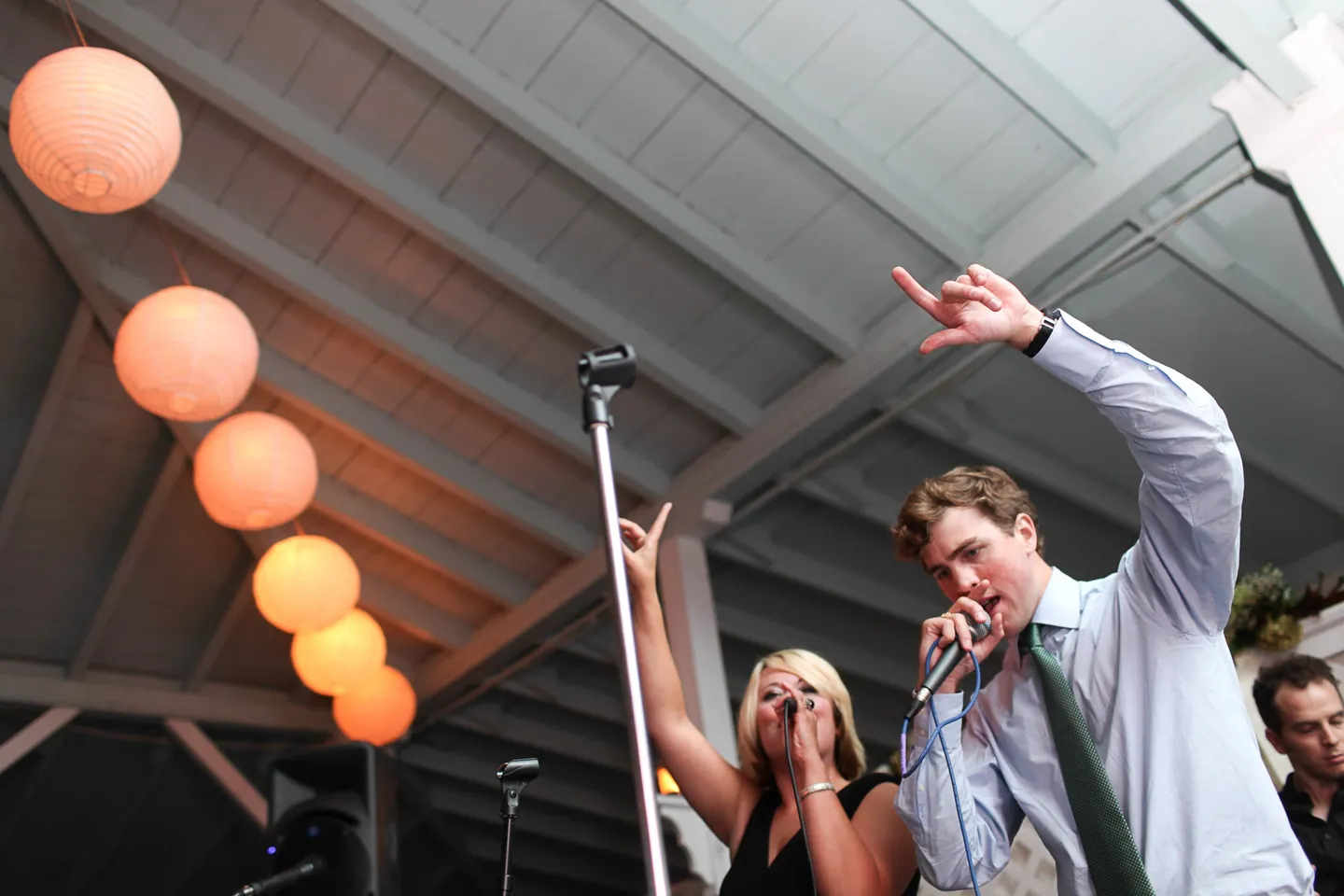 The groom sings into a microphone beside the band's singer under glowing paper lanterns